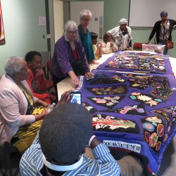 women sitting around a table, looking at the quilt they have made